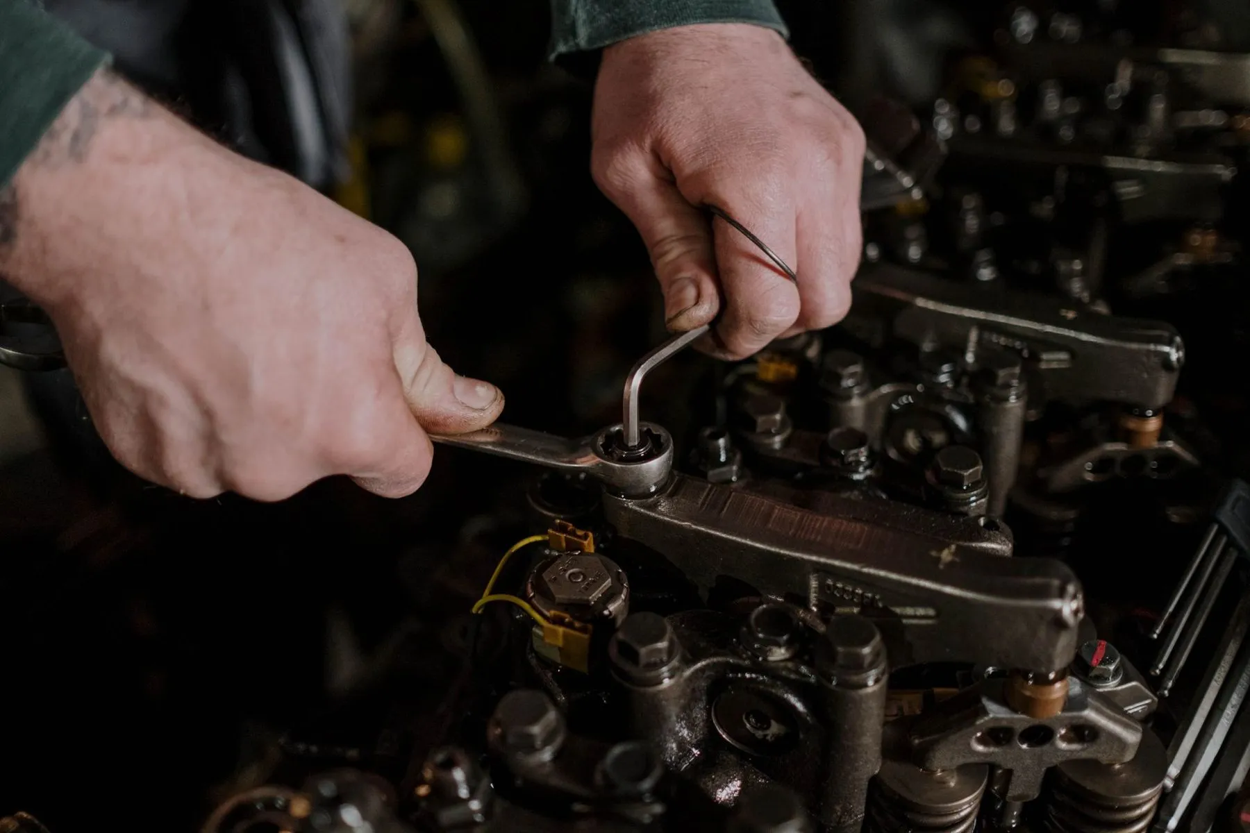 Two hands working a ring spanner on an engine