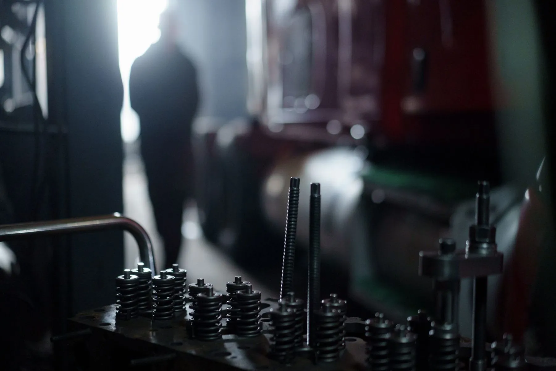 A technician walking into the workshop past a bench of valve springs
